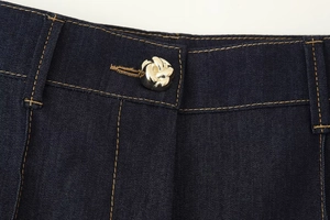 Gros plan des coutures contrastées blanches et bouton argenté sur veste en jean bleu