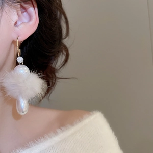 Detail of elegant C-shaped earring with white fur ball and pearls on a model ear