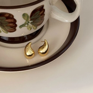 Macro view of polished gold teardrop stud earrings with smooth metallic finish