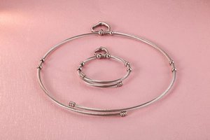 Detail of silver cable wire jewelry set with heart charms on pink leather background