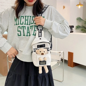 Detailed view of white canvas chest bag with a cute plush bear accessory on a model