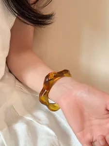 Detail of translucent amber acrylic wide bangle with irregular wave design worn on wrist