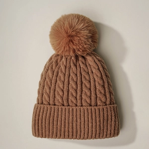 Close-up of brown cable knit beanie showing thick texture and soft faux fur pom-pom detail