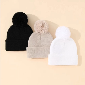 Tre cappelli di maglia per bambini nei colori nero, beige e bianco con grandi pompon