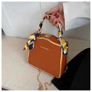 Detail of brown leather box bag featuring a printed silk scarf handle and metal chain strap