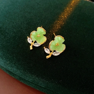 Detailed macro of gold-plated flower earring with green petals on dark velvet