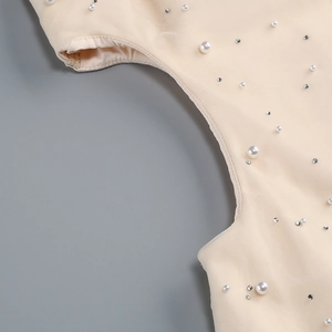 Detail of apricot mesh fabric featuring hand-sewn pearls and rhinestones on the dress