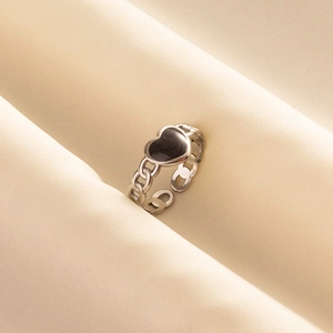 Detail of silver chain ring featuring a black hollow heart on soft beige fabric