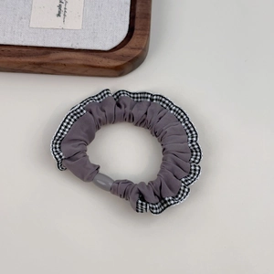 Gray-purple scrunchie with houndstooth lace edge and grey bead on a beige background