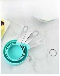 Detail of four green measuring cups with stainless steel handles on marble surface