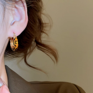 Close-up of a 14k gold plated leopard print hoop earring worn by a model in soft warm lighting