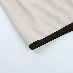 Detailaufnahme des beigen Kleidsaums mit schwarzer Kontrastpaspel und Doppelnähten