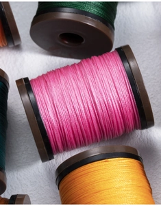 Close-up of vibrant 0.4mm round waxed threads in pink, yellow, and green spools
