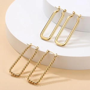Golden U-shaped earrings in polished and twisted textures on white geometric stands