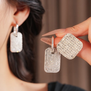 Macro detail of silver square hoop earrings with shimmering pavé crystal rhinestones