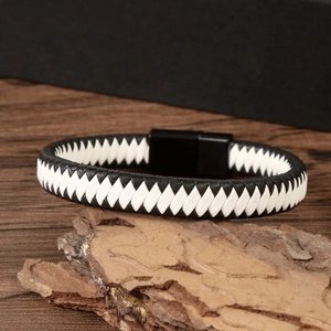 Detailed view of woven black and white leather bracelet on a rustic wood block background