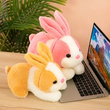 Pink and orange plush sheep toys resting on a desk near a laptop in a cozy indoor setting