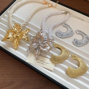 Detail of chunky gold and silver flower pendant necklaces and twisted hoop earrings