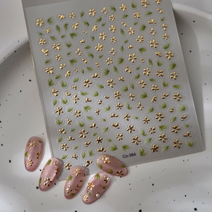 Detail of 3D gold floral nail stickers with green leaves and embossed texture on pink nails