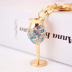Elegant gold wine glass keychain with sparkling blue and white rhinestones on white books