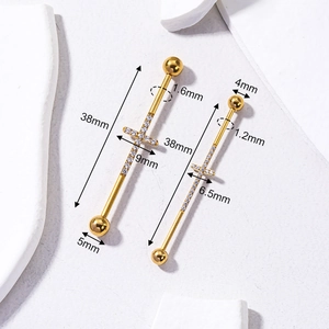 Piercings industriel en acier doré avec croix en zircon sur un fond blanc texturé