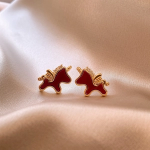 Gros plan de boucles d'oreilles licorne en émail rouge et cristaux sur fond de soie