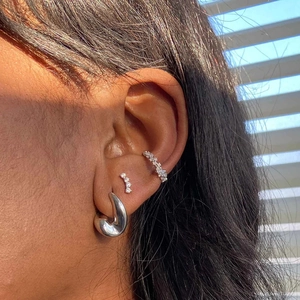 Dettaglio di orecchini a cerchio d'argento e ear cuff con cristalli sulla modella