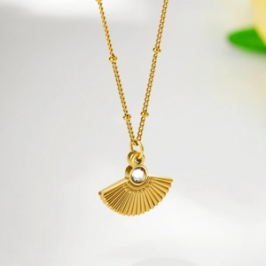 Close-up of golden fan-shaped pendant with round zircon inlay and beaded chain necklace
