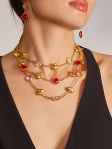 Detalle de collar multicapa de oro de 18K y pendientes de corazón con gemas rojas