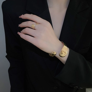 Polished gold-plated wide open bangle and ring set worn against a black suit