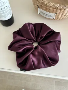 Close-up of large burgundy satin scrunchie with fashion label and glossy texture