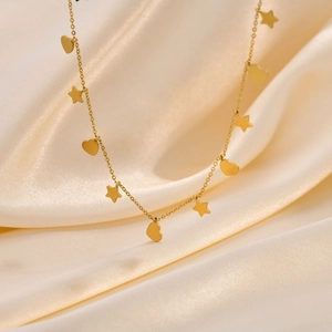Dettaglio della collana dorata con ciondoli a cuore e stella su seta beige morbida