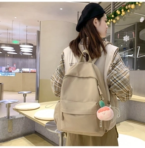 Lifestyle view of khaki nylon backpack with peach plush charm and side pocket details