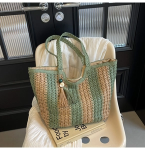 Close-up of a green striped woven straw tote bag with a tassel charm on a white chair