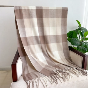 Detail of a beige and brown plaid scarf with fringe draped on a beige armchair