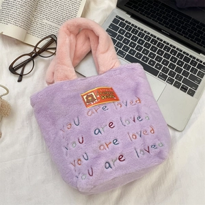 Gros plan sur un cabas en peluche mauve à poignées roses et broderie de texte coloré