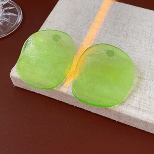 Detailed close-up of green translucent oval earrings with texture on a beige linen surface