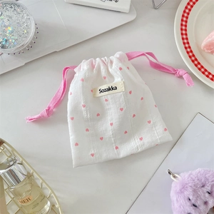 Close-up of a white fabric drawstring pouch with pink heart prints and woven label