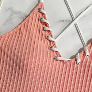 Close-up of pink ribbed swimsuit with lace-up V-neck and metal eyelet details