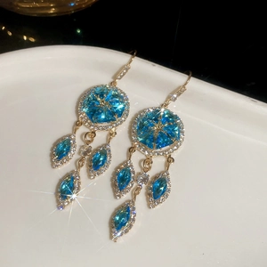 Detail of gold-plated earrings with marquise-cut blue crystals on white porcelain