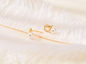 Macro view of gold S925 silver twist pearl earrings resting on a white feather
