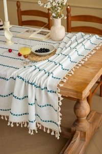 Close-up of white linen tablecloth featuring blue leaf patterns and beige tassel fringe