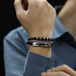 Detail of multi-layer men's braided leather bracelet with black beads and metal plate
