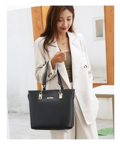 Close-up of black tote bag with gold hardware and logo on a white suit model