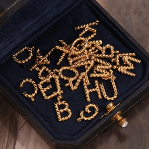 Macro view of 18K gold plated rope textured alphabet pendants in a blue velvet box