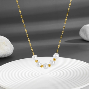 Minimalist titanium steel necklace with white pearls and gold beads on a white tray