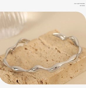 Macro shot of silver wave-shaped geometric open bangle resting on natural stone