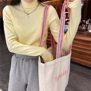 Detail of canvas tote bag with pink smile embroidery and yellow ribbed knit sweater