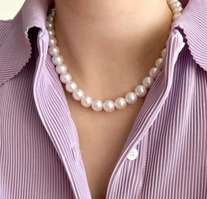 Detailed view of an 8-10mm white round pearl necklace worn with a purple pleated shirt