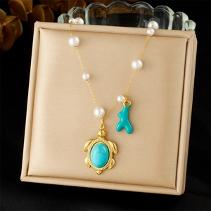 Collana tartaruga dorata con ciondolo turchese e corallo su espositore di velluto beige